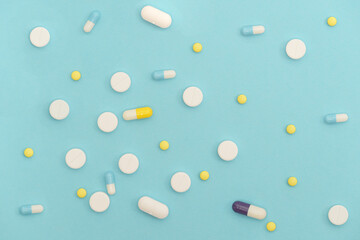 Medicine capsules, pills and tablets on light blue background.