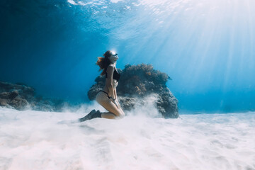 Freediver slim woman with fins posing over sandy bottom underwater sea