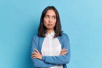 Portrait of displeased offended young Asian woman with dark hair keeps arms folded looks angrily...