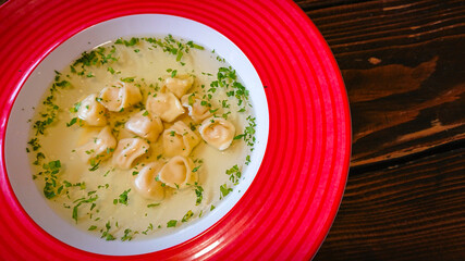Red plate with broth and dumplings on the table
