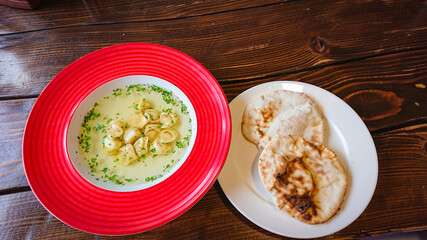 Red plate with broth and dumplings on the table
