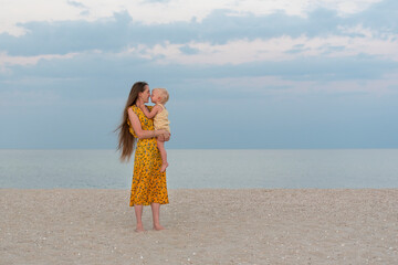 Mother and child on sandy beach on sea and sky background. Maternal care and love. Seaside holiday...