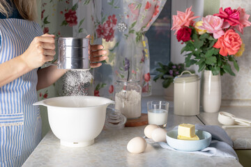 housewife sifting flour into bowl. Ingredients for making dough on kitchen table. Cooking and baking concept. close-up.