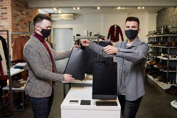 A man in a face mask to avoid the spread of coronavirus is taking his purchases in a clothing...
