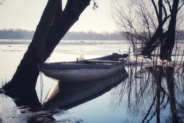 boat reflecting in the water moored by a tree on a partially frozen Vistula river in Poland