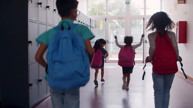 Schoolkids of different ages leaving school, running and hopping to entrance door in hall. Dolly shot, back view. Education or childhood concept