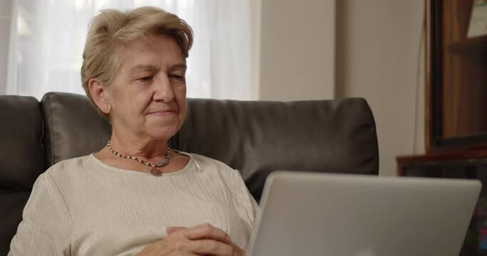 Older women have to work from home with online training meetings on a laptop and she was in a comfortable position leaning on the sofa at her home alone.