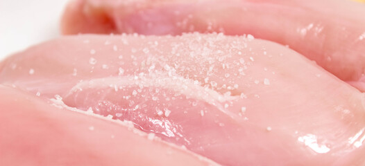 Raw chicken fillet close-up, on which salt is sprinkled on top.