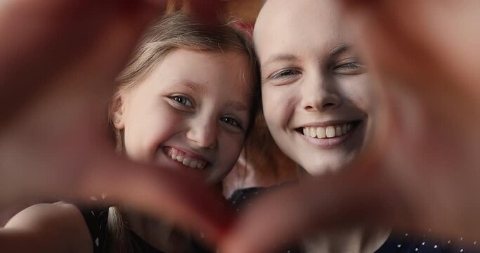 Little adorable girl her young bald mother making heart shape with hands showing symbol of love at camera, close up view happy faces. Share support optimism and hope with other cancer patients concept