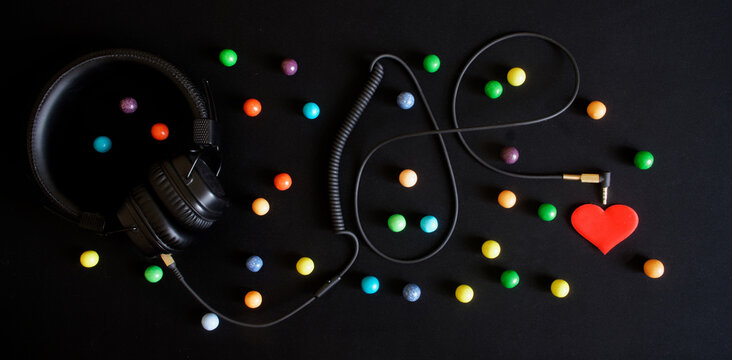 Wired headphones, multicolored balls and a red heart on a black background. Audiophilia and a variety of emotions evoked by music.