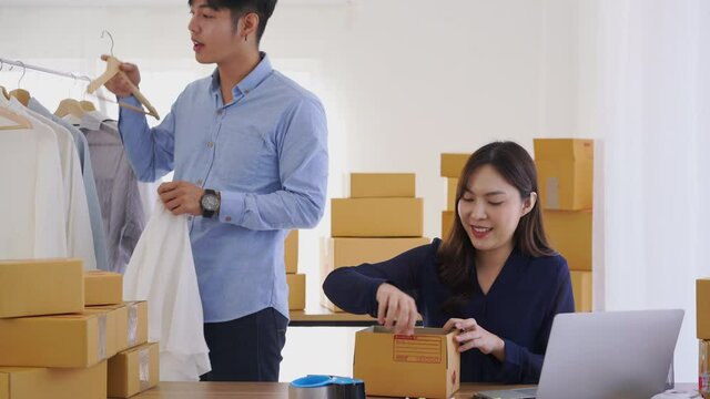 Asian young couple selling clothes product online and packing parcel box at home office