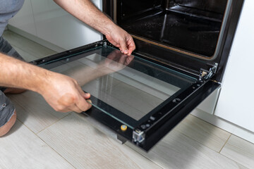 a man disassembles the door of a dirty oven for cleaning