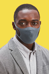 Vertical head and shoulders portrait of African-American man wearing mask and looking at camera while standing against pop yellow background