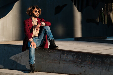 Hipster man dressed stylishly sitting outdoors.