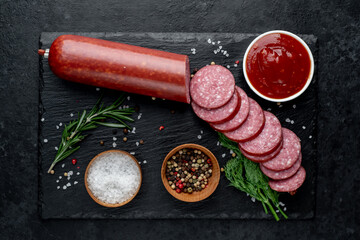 Dry salami sausage with fresh rosemary and spices on a stone background  - obrazy, fototapety, plakaty