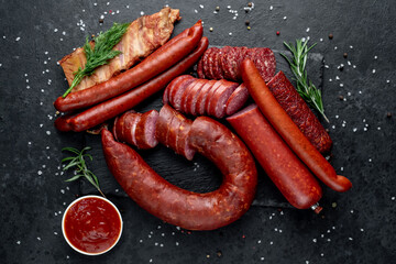 Set of sausages, salami and smoked meats with rosemary and spices on a stone stone background. View...