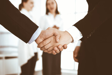 Businessman and woman shaking hands with colleagues at the background. Handshake at meeting in office. Concept of success in business