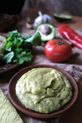 Delicious plate of traditional Mexican guacamole and ingredients guacamole, avocado, pepper, tomato, garlic, cilantro, arugula. Top view, flat lay. Fresh, raw, vegetarian dish. 