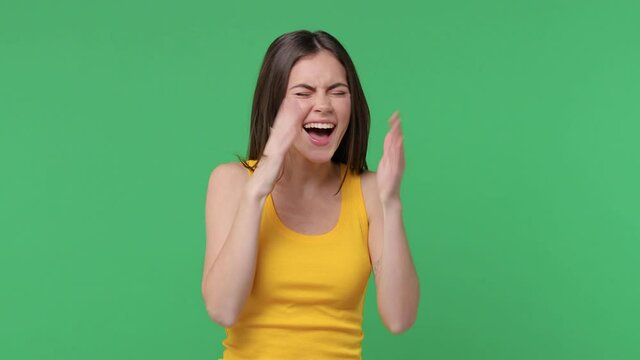 Excited laughing brunette young woman 20s years old in yellow basic tank top posing isolated on green color background in studio. People emotions lifestyle concept. Pointing index finger camera on you