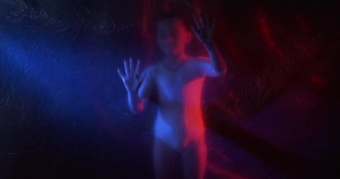Child protection. Defocused silhouette. Pandemic self isolation. Curious small ballerina girl touching creased texture transparent polyethylene film on dark red blue neon light out of focus.
