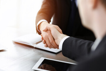 Businessman shaking hands with his colleague above the glass desk in sunny modern office, close-up. Unknown business people at meeting