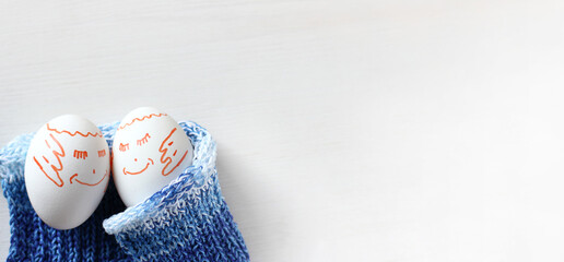 pair of chicken eggs with painted cheerful faces sleep on a blue knitted blanket. have happy dreams together