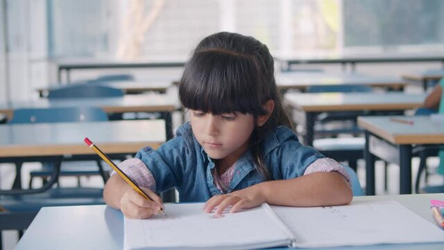Focused primary school pupil girl holding pencil and drawing in album or copybook at desk in classroom. Childhood or education concept
