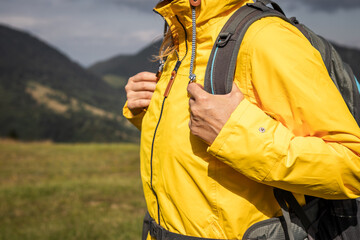 Sports clothing for extreme weather. Woman with backpack hiking in mountain and wearing yellow waterproof jacket