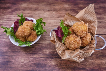 CROQUETAS  CASERAS DE JAMÓN PREPARADAS EN UN CUBITO BLANCO Y SOBRE UN FONDO DE MADERA