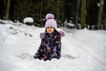Fototapeta na wymiar beautiful girl in a purple hat plays in the snow on a forest background