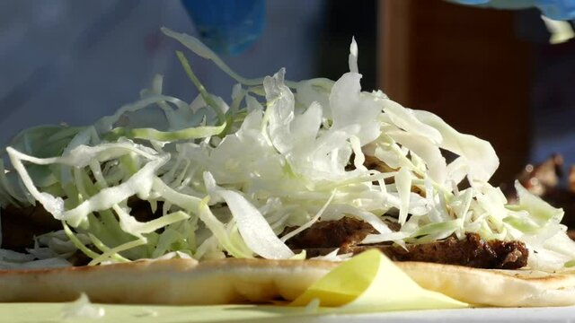 Close up of a chef adding shredded cabbage to a gyros sandwich
