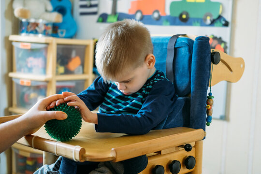 Sensory Activities for kids with disabilities. Preschool Activities for Children with Special Needs. Boy with with Cerebral Palsy in special chair play with mom at home.