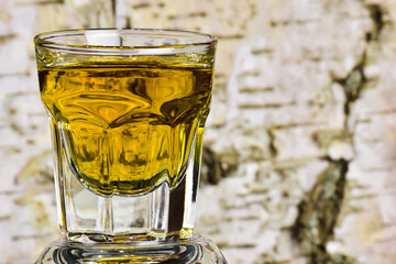 On the background of birch bark on the left side, a close-up of a glass of whiskey or brandy. On...