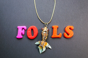Fototapeta na wymiar The word fools made of colored letters with a gold fish on a black background. April Fools' Day. April Fool's Day. Fish day