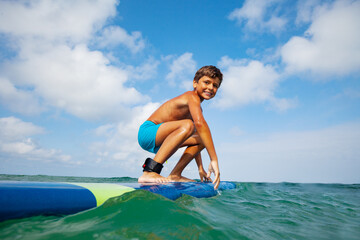 Low angle photo of a boy squatting on the surfboard prepare to ride the wave © Sergey Novikov