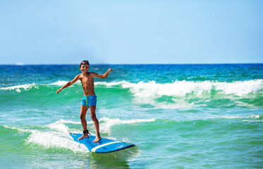 Little boy confidently ride waves on surfboard happy smiling and looking to camera