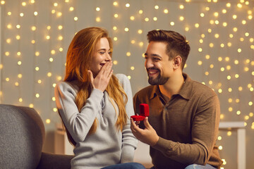 What a surprise. Couple in love enjoying romantic evening together. Happy smiling man proposing to girlfriend and giving her gold engagement ring. Young woman getting and accepting marriage proposal