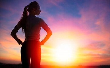 The silhouette of young sporty woman watching the sunset background
