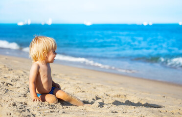Handsome cute little blond boy sit on the beach near the sea
