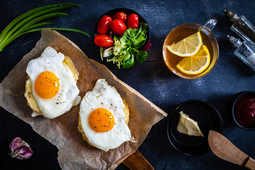 Continental breakfast - sunny side up eggs on baked bun with cheese and vegetable salad on black background
