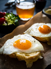 Continental breakfast - sunny side up eggs on baked bun with cheese and vegetable salad on black background
