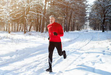 Athletic mature man in sportswear jogging at snowy winter park. Healthy senior runner sprinting...