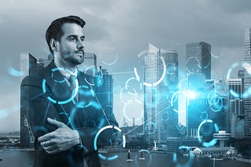 A young Caucasian businessman in crossed arms pose pondering on technology at business process to achieve tremendous growth. Tech hologram icons over Singapore background