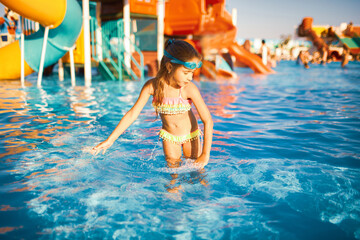 Cheerful girl in a bright bathing suit and blue swimming goggles is spinning in a pool with clear water with her hands in the water