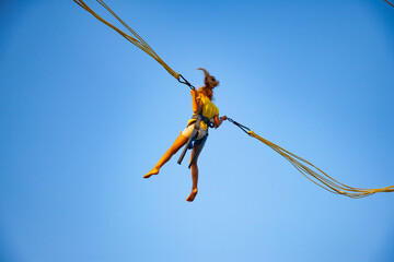 A little cheerful girl flies on springy bright elastic bands and jumps on a trampoline enjoying the long-awaited vacation in the warm sun