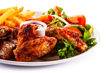 Roast chicken wings with curly fries and vegetable salad on white background
