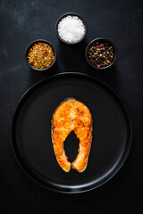 Fried salmon steak with seasonings served on black background