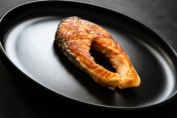 Fried salmon steak served on black background