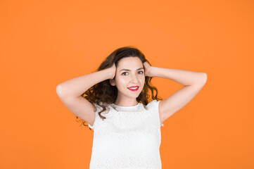 Portrait of smiling young woman standing with hands in hair against orange background. Caucasian girl with red lips looking at camera