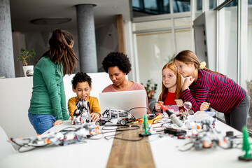 Happy kids with their African American female science teacher with laptop programming electric toys and robots at robotics classroom